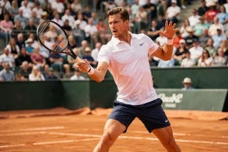 Joueur de tennis professionnel en plein revers puissant sur un court en terre battue lors d'un grand tournoi 2026